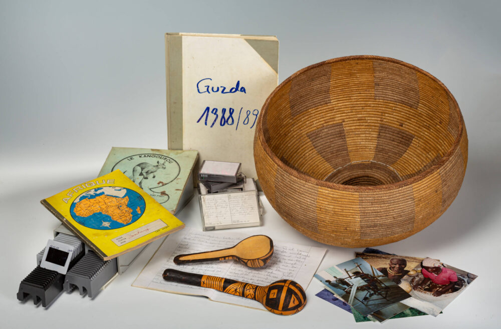 Verschiedene Gegenstände wie Fotos, Diakästen, Rasseln, Notizbücher und ein Korb einer Forschungsdokumentation.