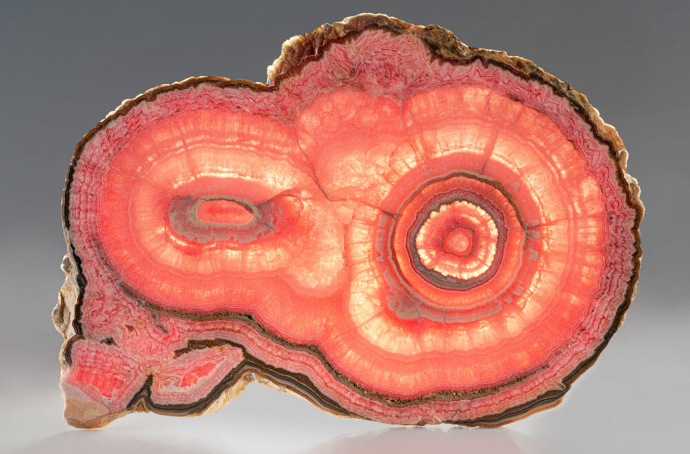 Dünne und lichtdurchlässige Scheibe des in verschiedenen Rottönen leuchtenden Minerals Rhodochrosit.