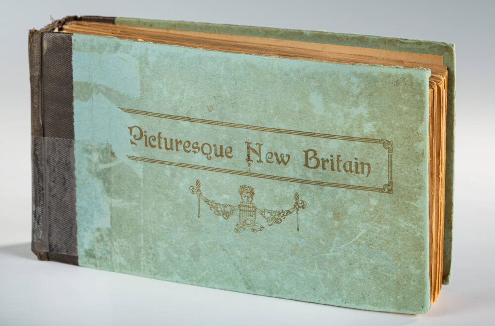 Fotoalbum mit vergilbten Seiten, einem hellblau-grünlichen Einband und einem schwarzen Buchrücken.