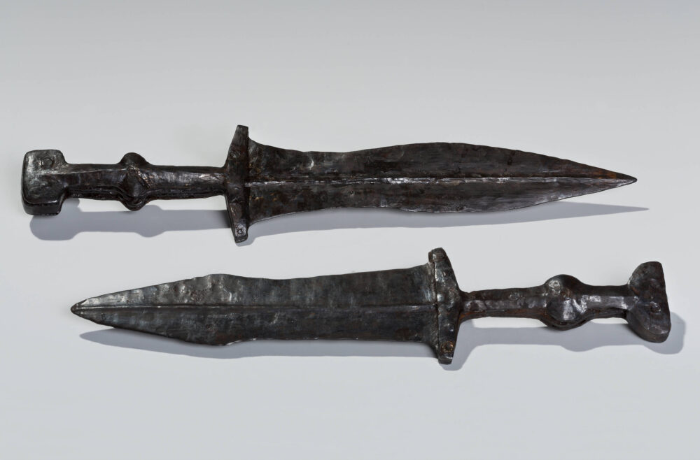 Zwei römische nahezu schwarze Eisendolche liegen auf weißem Untergrund.