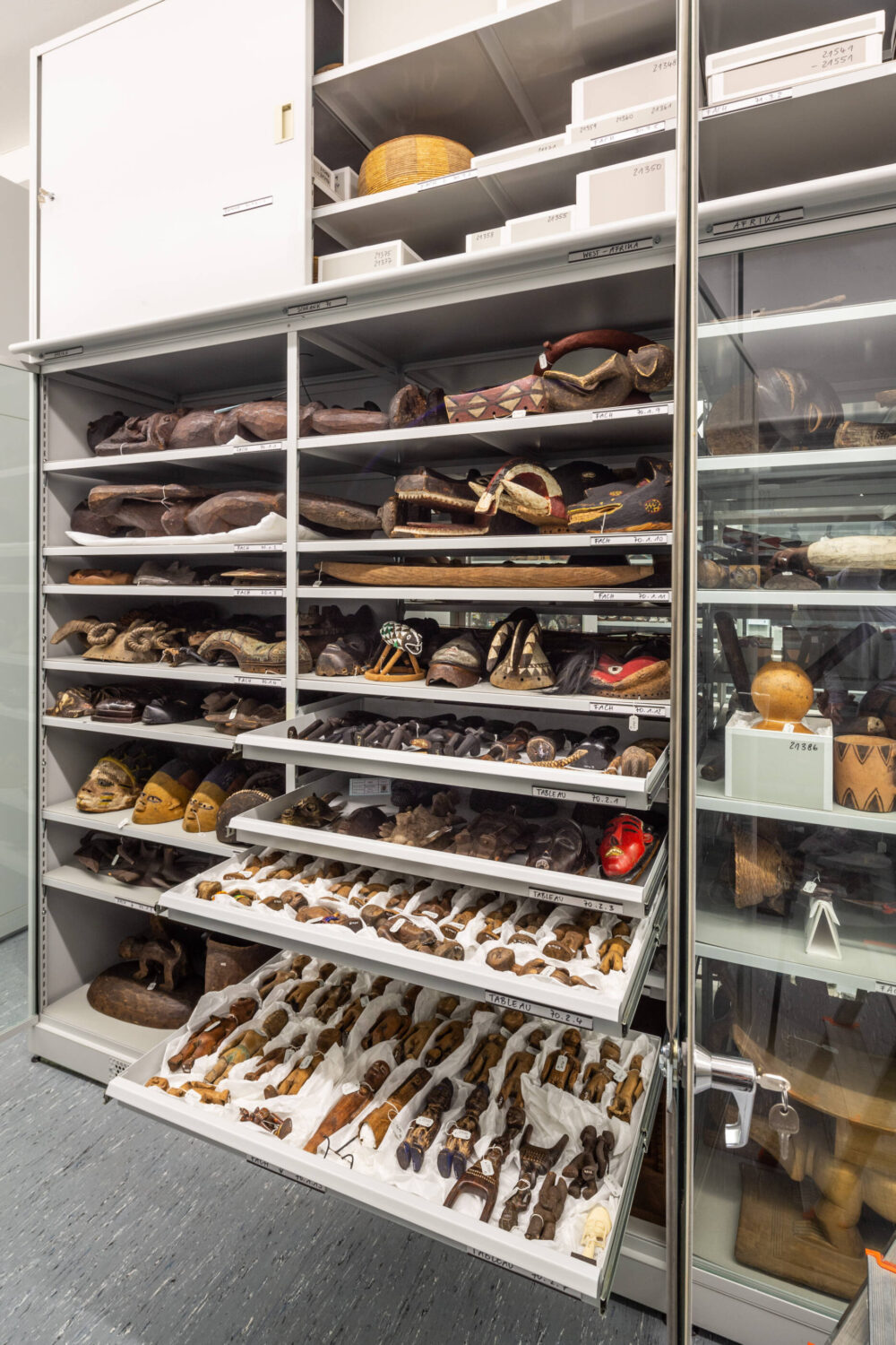 Blick in einen geöffneten Depotschrank mit verschiedenen westafrikanischen Objekten in Fächern und Schubladen.