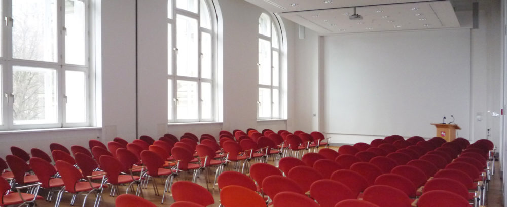 Der mit roter Bestuhlung ausgestattete Vortragssaal des Landesmuseums mit Rednerpult auf der rechten Seite im Hintergrund.